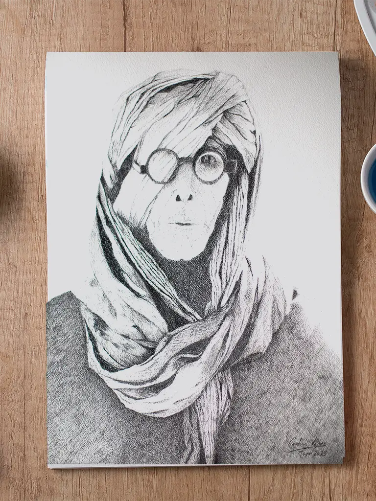 Retrato en grafito de una persona con gafas y la cabeza envuelta en telas, sobre papel colocado sobre una mesa de madera.