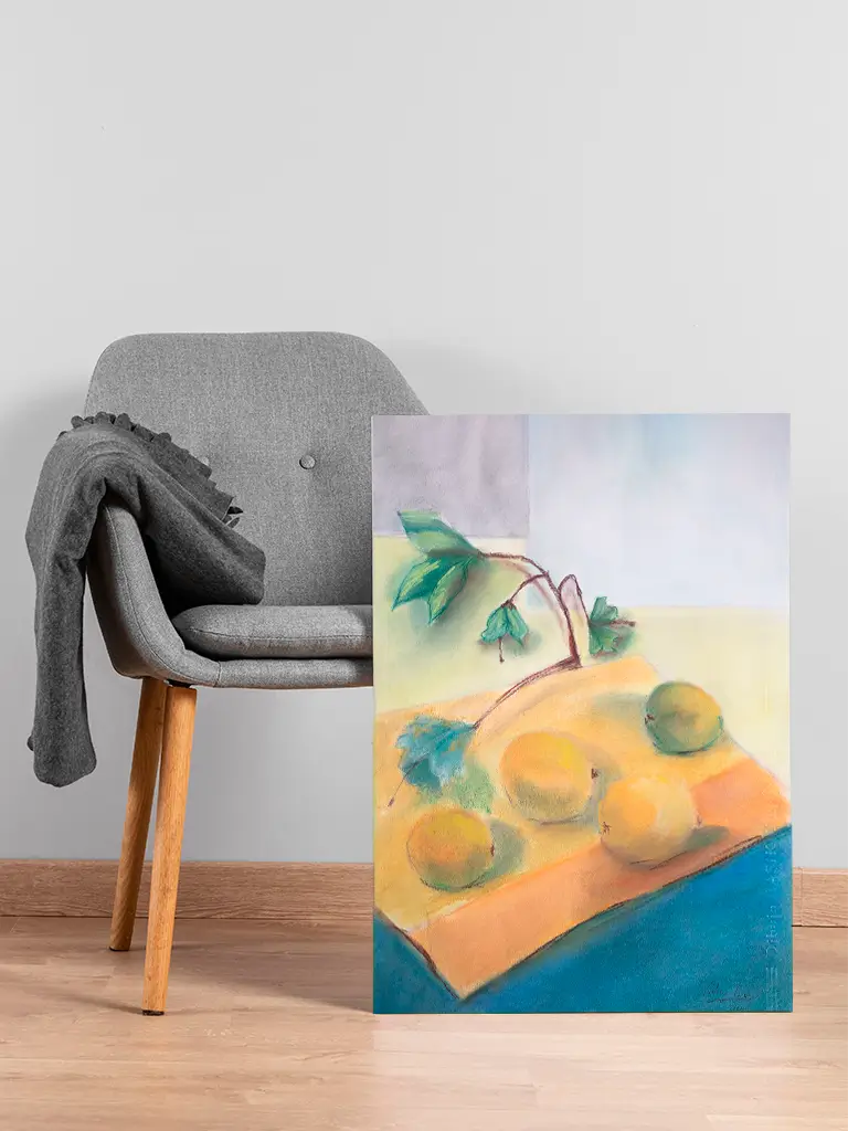 Pintura al pastel de un bodegón con limones y ramas verdes sobre un mantel, apoyada en el suelo junto a una silla gris.