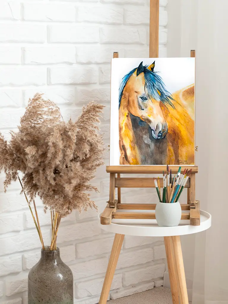 Pintura de un caballo en acuarela sobre un caballete de madera con pinceles y decoración natural