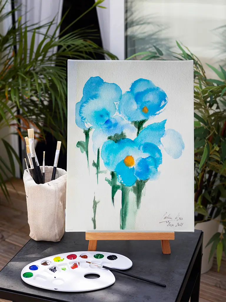 Pintura en acuarela de flores azules con centro amarillo sobre un caballete artístico